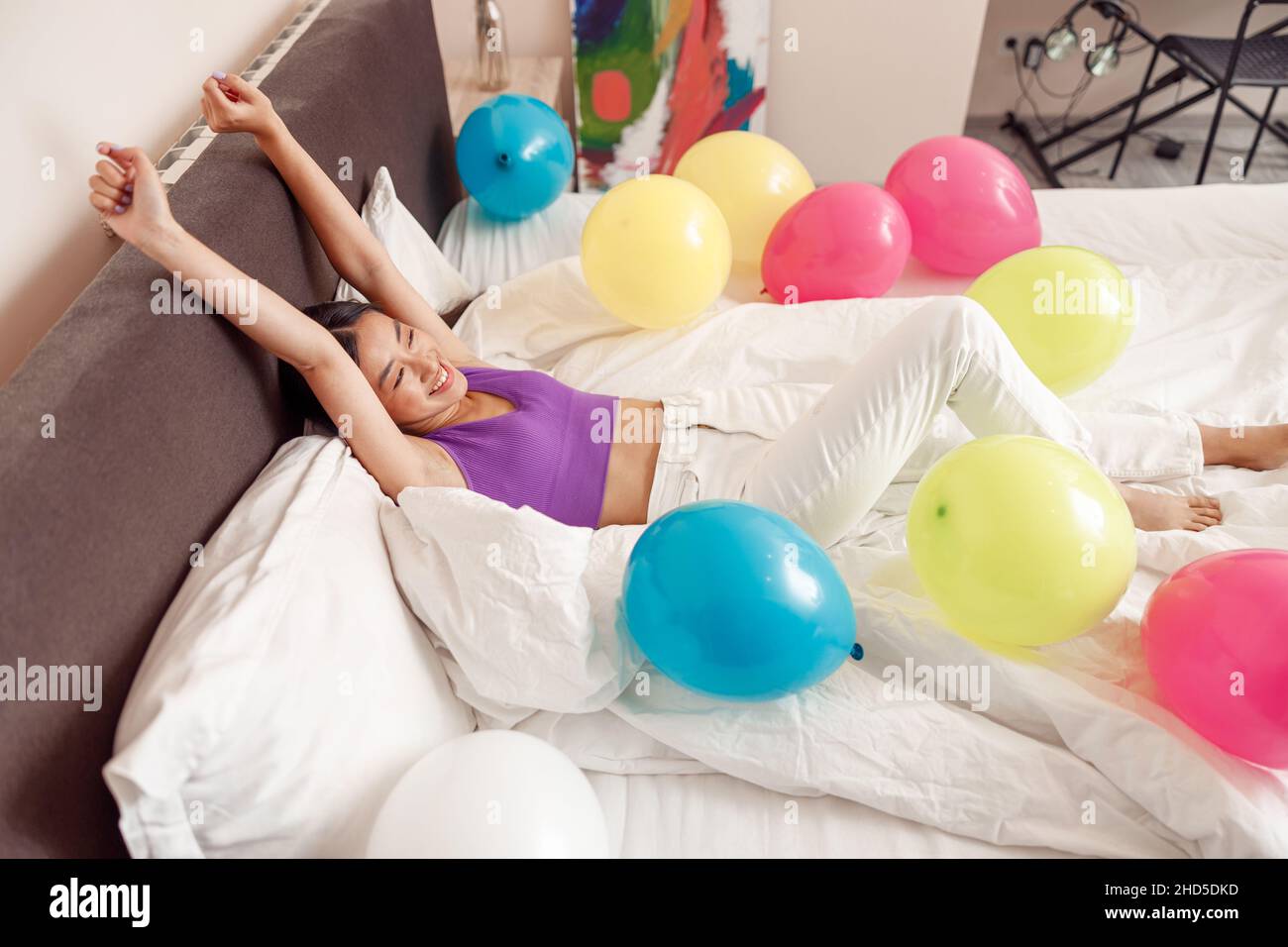 Glückliche junge Frau, die im Bett mit bunten Luftballons liegt Stockfoto