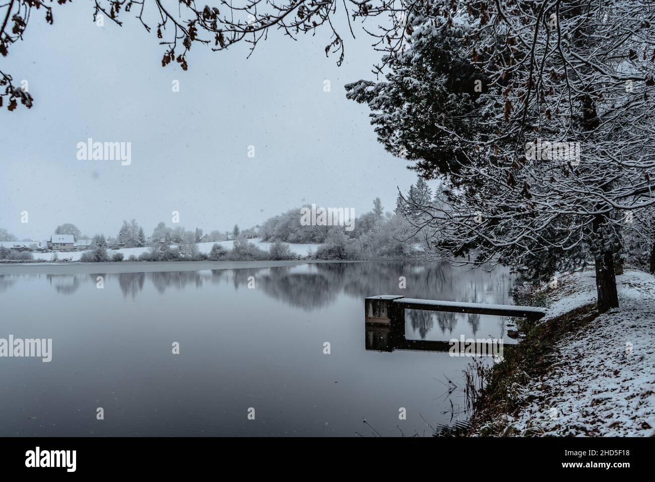 Hölzerner Pier am See mit frischem Schnee.Winterteich mit kleinem Steg am nebligen Morgen.Foggy bewölkte Landschaft im Wasser reflektiert. Weiße Winterlandschaft Stockfoto