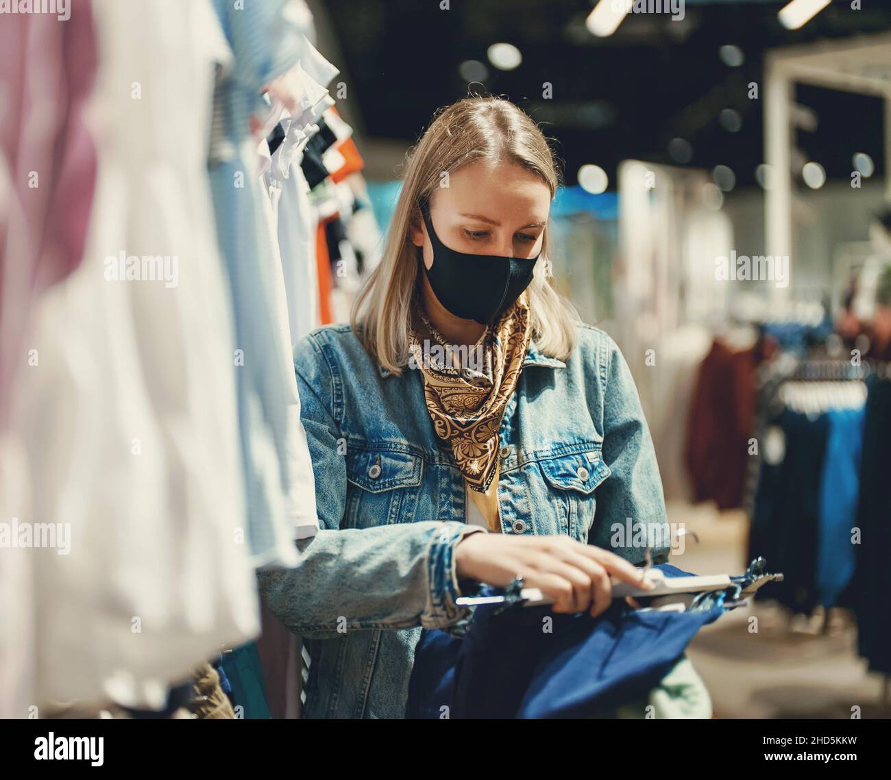 Frau in medizinischer Maske Wahl Kleidung im Outlet Store. Stockfoto