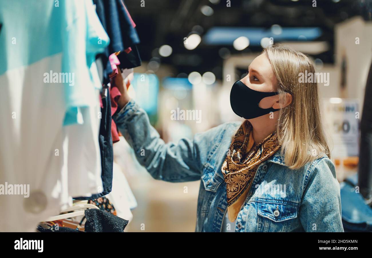 Frau in medizinischer Maske Wahl Kleidung im Outlet Store. Stockfoto