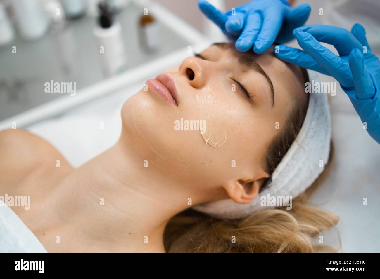 Die Hände des Kosmetologen tragen Creme auf das Gesicht der Frau auf. Frau massiert die Gesichtshaut des Kunden Stockfoto