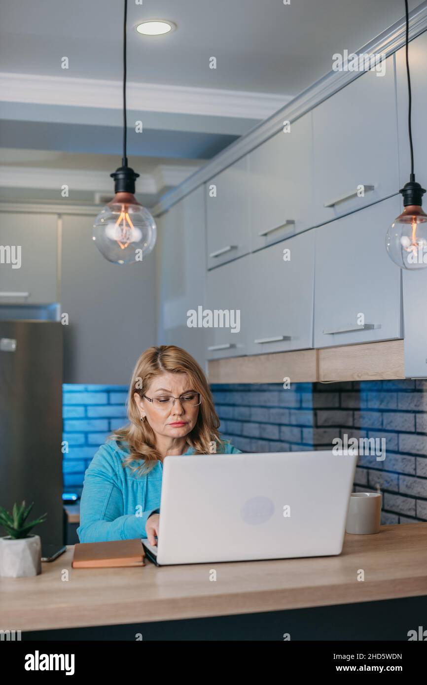 Porträt einer Frau mittleren Alters, die in Innenräumen an einem Laptop arbeitet. Vorderansicht. 40s. Finanzielle Investitionen des Unternehmens. Porträt einer Geschäftsfrau. Unternehmenstechnologie Stockfoto