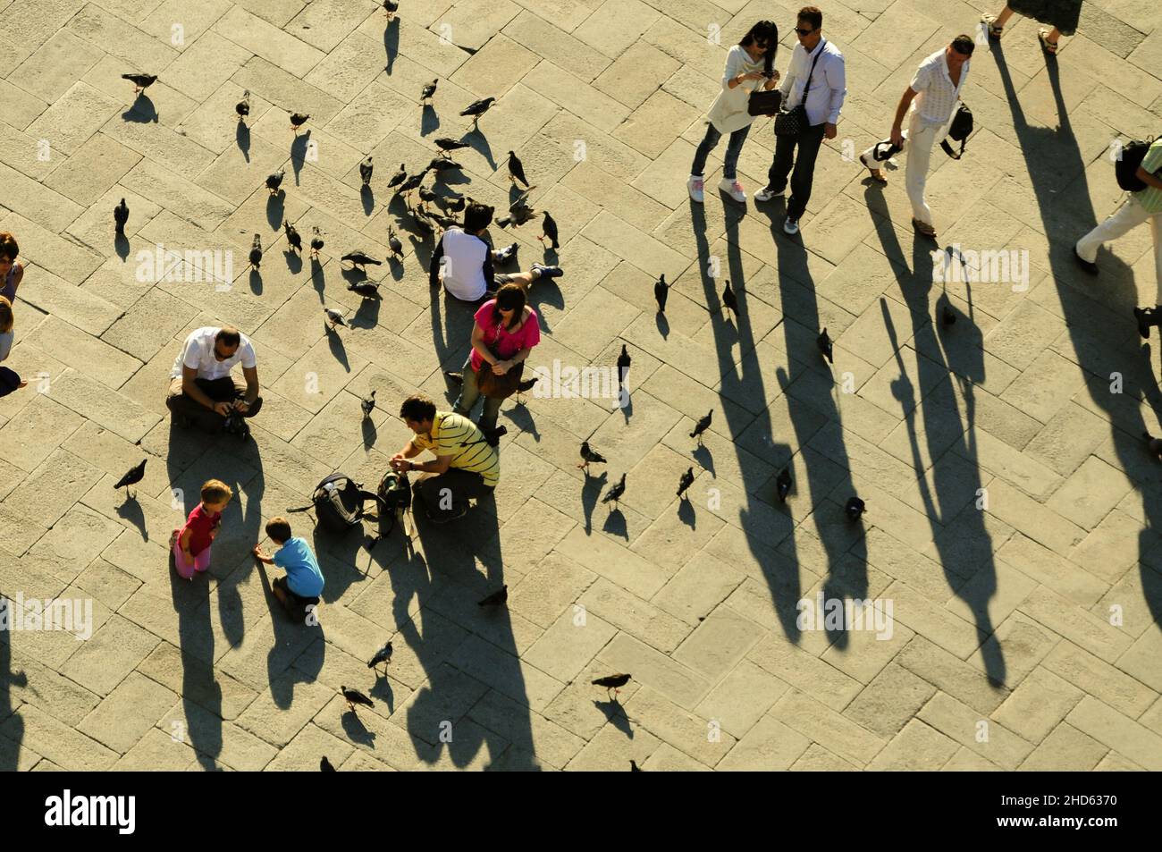 Touristen, die am frühen Morgen auf dem Markusplatz in Venedig mit Tauben spielen Stockfoto