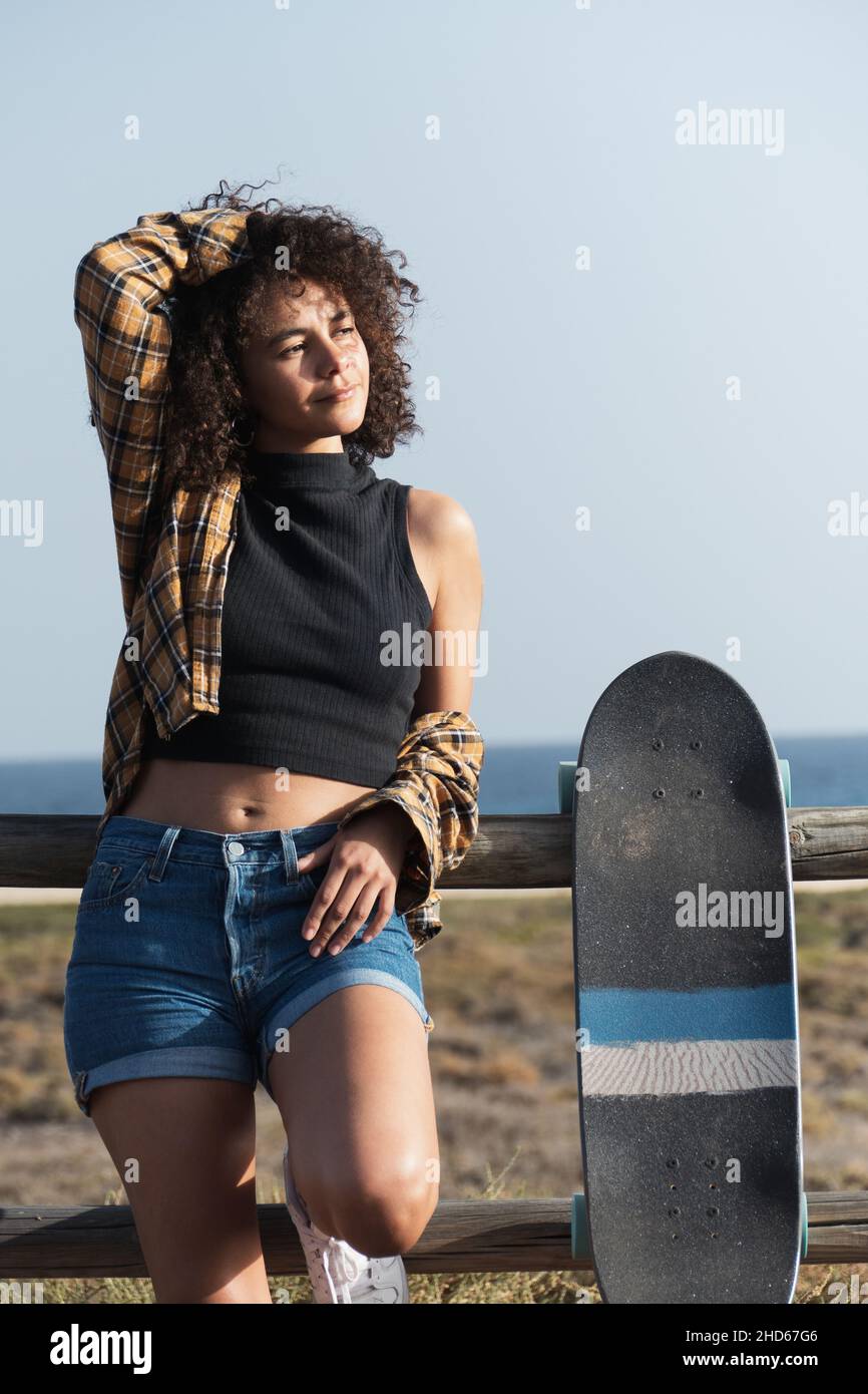 Attraktive junge Skaterin Frau mit afro Haar auf einem Zaun im Freien gelehnt Stockfoto