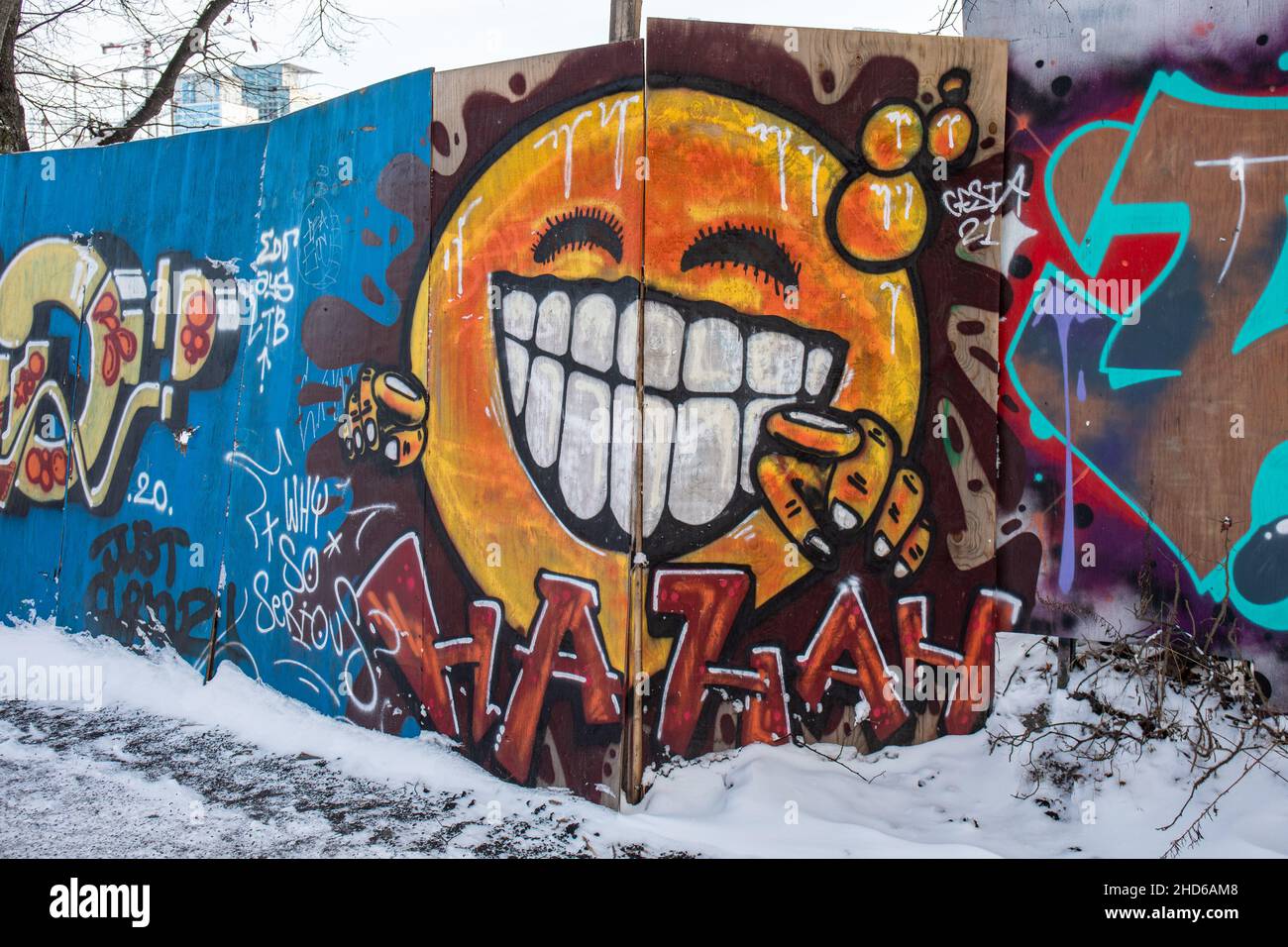 Straßenkunst. Lachende orangefarbene Wandgraffiti auf Baustellenzaun im Bezirk Suvilahti in Helsinki, Finnland. Stockfoto