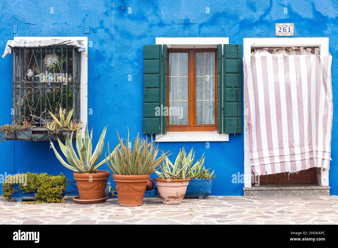 Nahaufnahme einer verwitterten hellblauen Gipsfassade mit Fenstern und einer Tür sowie Topfpflanzen auf dem Bürgersteig Stockfoto