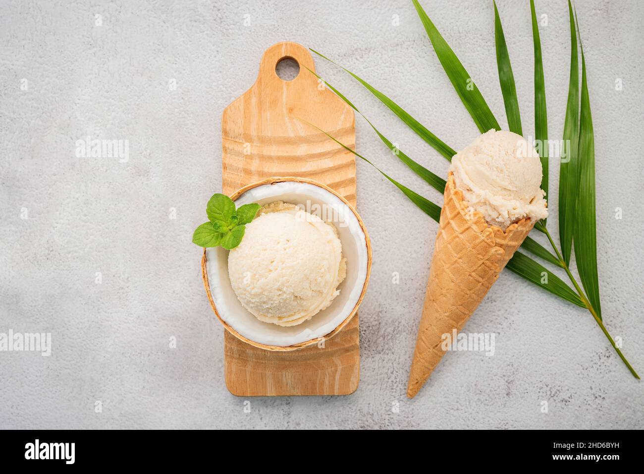 Kokoseis Aromen in der Hälfte der Kokosnuss Setup auf weißem Stein Hintergrund. Sommer und Süße Menükonzept. Stockfoto