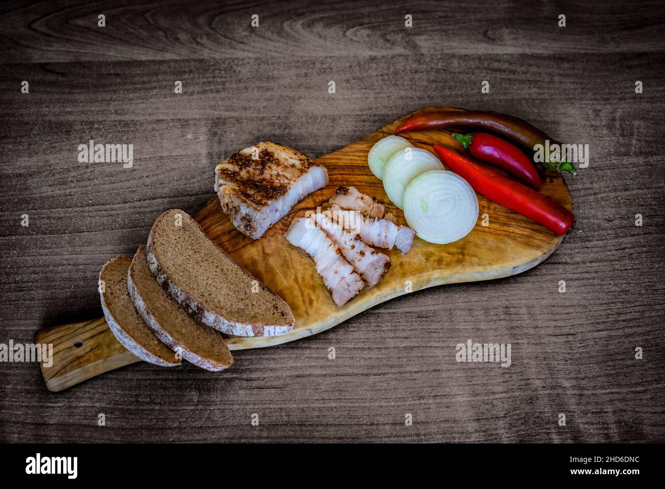 Vintage-Bild - Brotscheiben, würziger Speck, Zwiebeln und Chili auf einem Holzbrett. Stockfoto