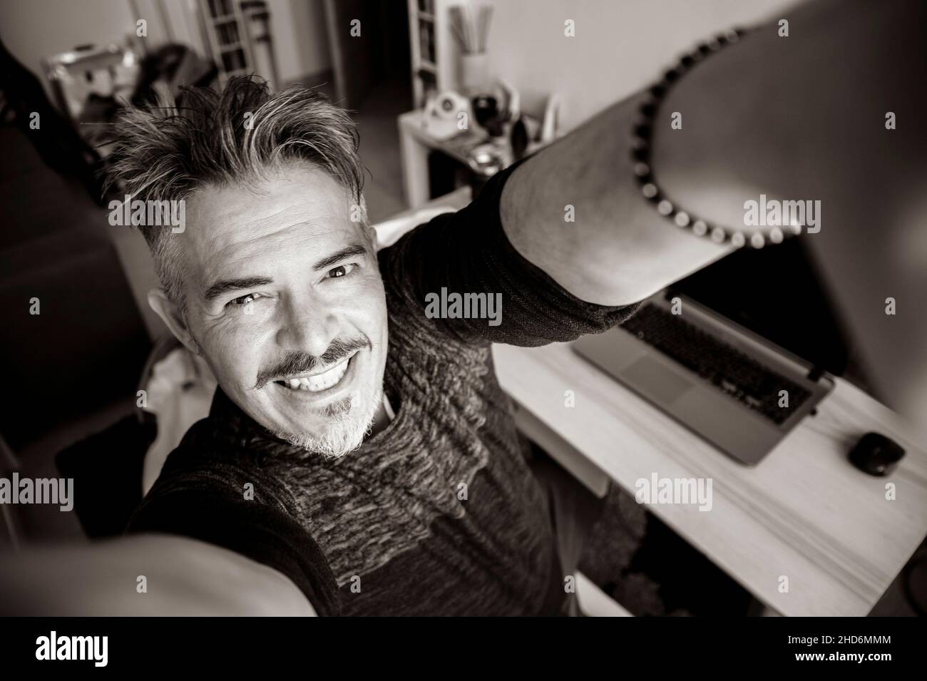 Hübscher kaukasischer 40-jähriger Mann, der zuhause ein Selfie-Porträt in der Halle nimmt - glücklicher Grizzled-Mann, der die Kamera anlächelt - Schwarz und Weiß Stockfoto