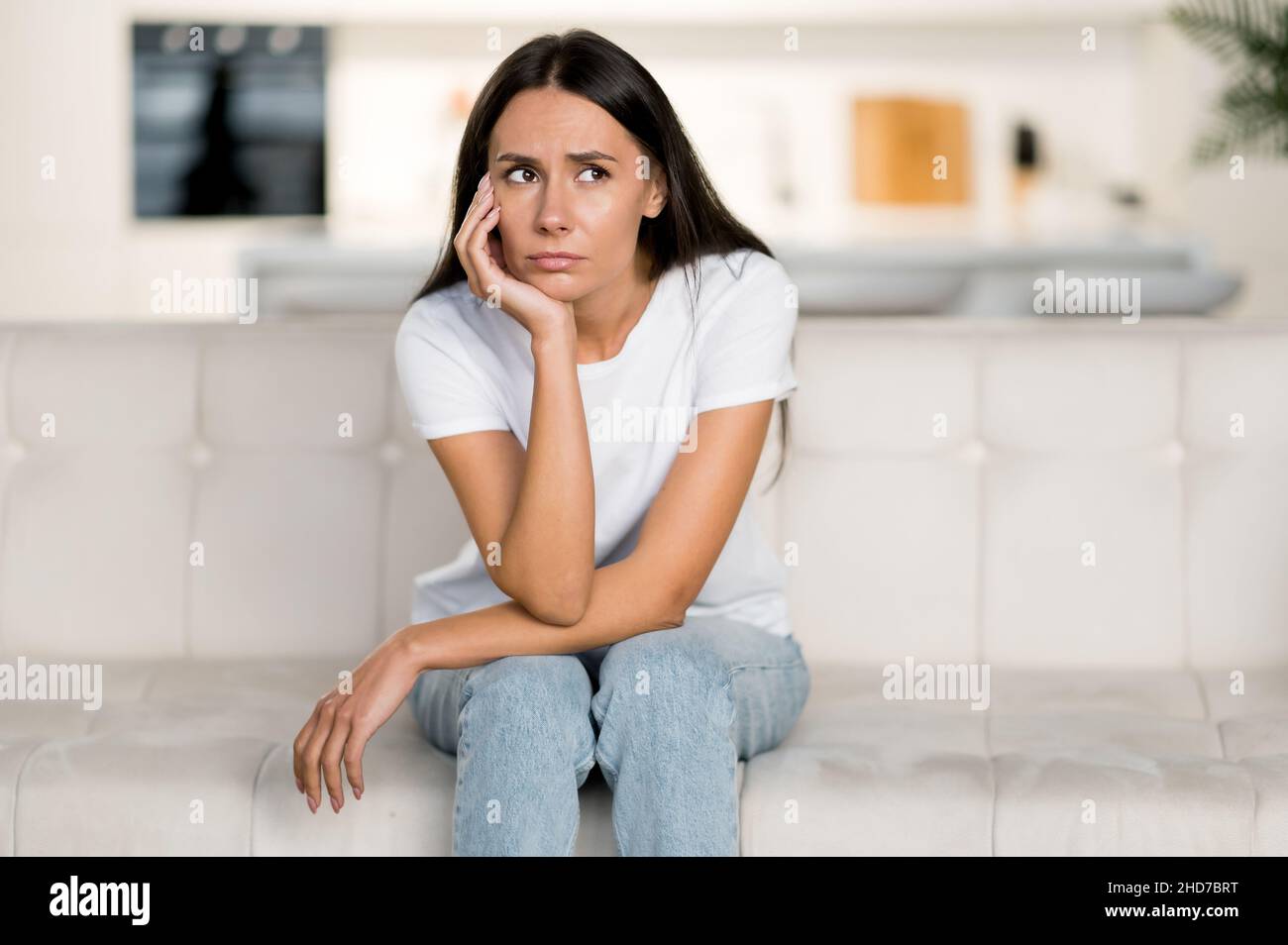 Enttäuscht unglückliche kaukasische junge Frau, die auf dem Sofa im Wohnzimmer sitzt, hat persönliche Probleme, Versagen bei der Arbeit, Depressionen, schlechte Laune, trauriges Mädchen ist zu Hause einsam Stockfoto