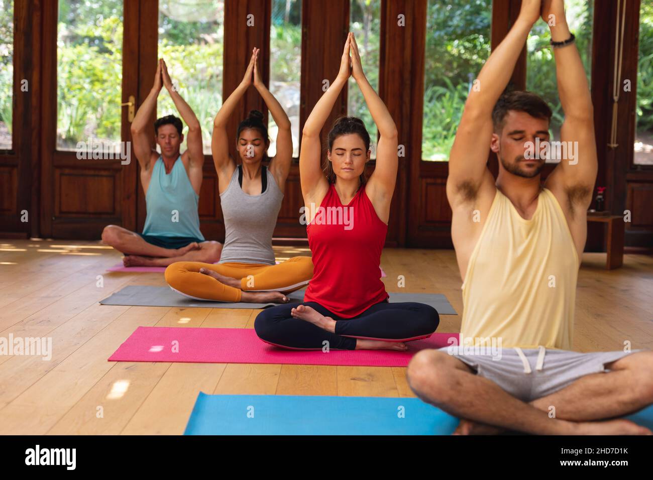 Männer und Frauen sitzen mit gekreuzten Beinen und Händen zusammengeschleppt und meditieren im Fitnessclub Stockfoto