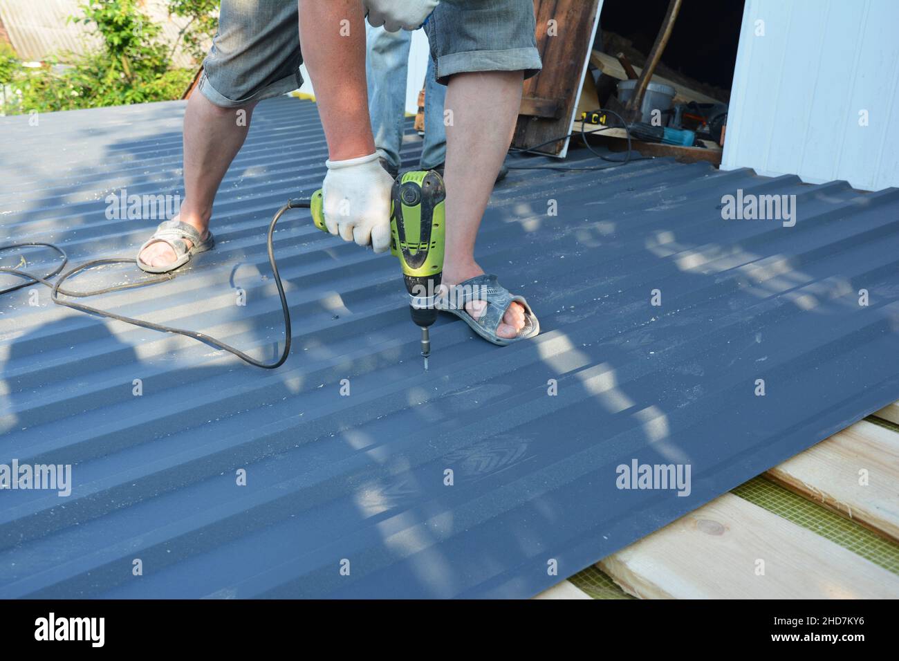 Eine Dachdeckerfirma installiert Metalldachpaneele und verschraubt Metalldachbleche mit einem Elektroschrauber an das Dachdeck. Stockfoto