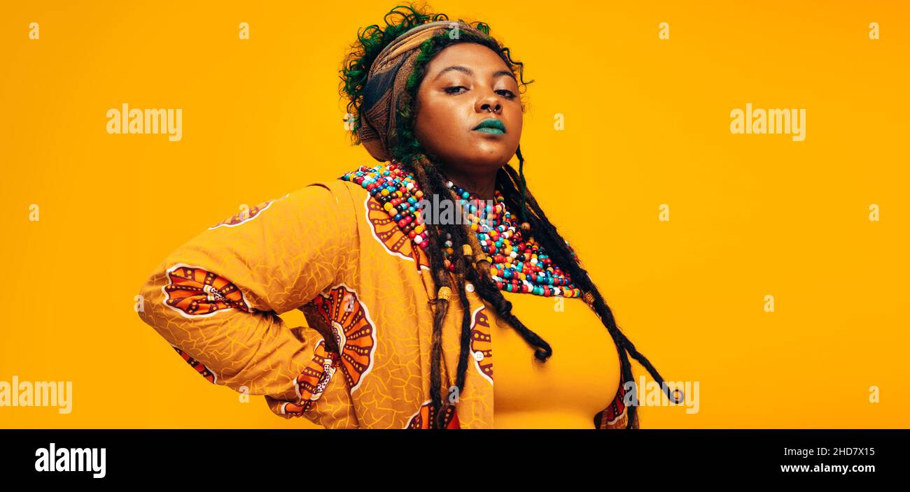 Selbstbewusste, starke Frau in traditioneller afrikanischer Kleidung. Modische junge Frau, die vor einem gelben Hintergrund auf die Kamera schaut. Stockfoto