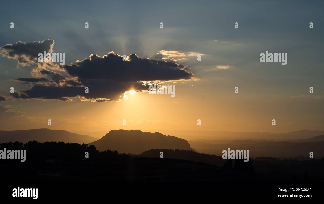 Herrliches Licht und herrliche Sonnenstrahlen, während die Sonne kurz vor Sonnenuntergang aus einer Wolke über den Hügeln und Tälern spaniens valenciana späht Stockfoto