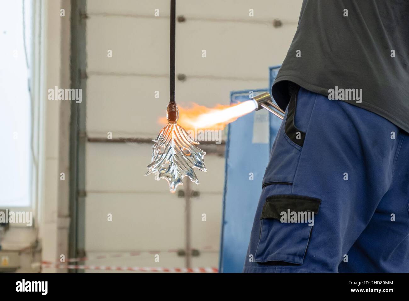 Ein Mann verwendet einen Gasbrenner, um Glas zu schmelzen. Ein Handwerker macht ein Glas in Blattform. Stockfoto