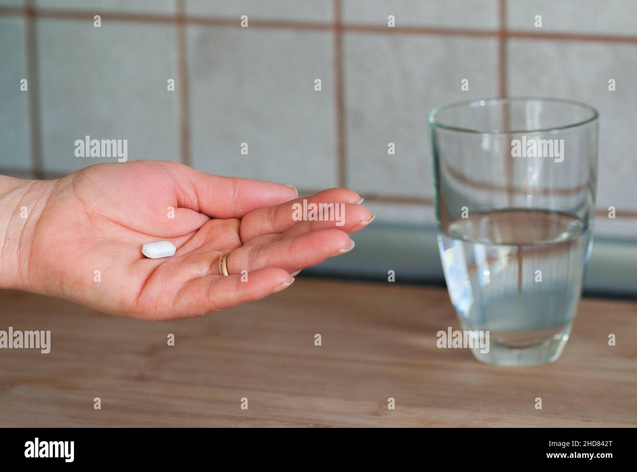 Frau hält eine Pille in der Hand und im Hintergrund ein Glas Wasser Stockfoto