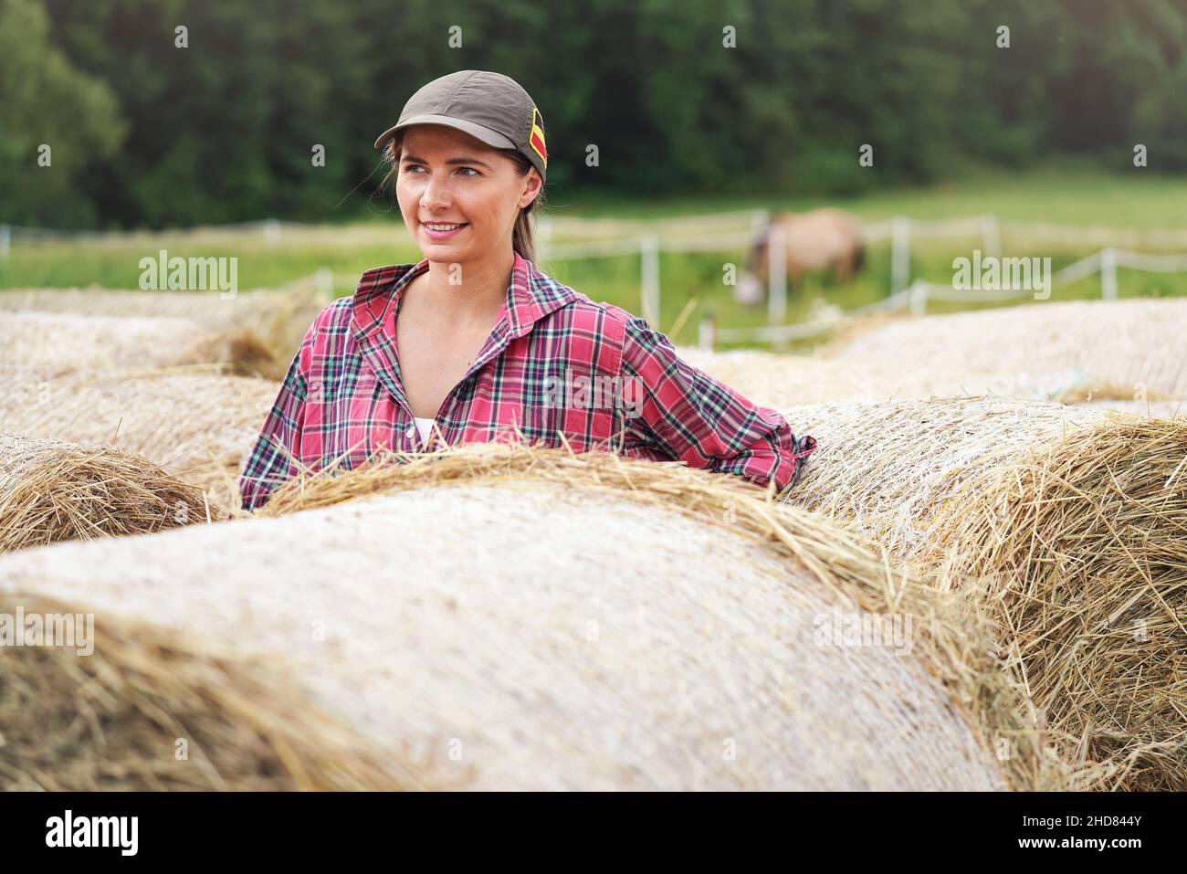 Junge Frau in Hemd und Mütze lächelnd, Heustapel rollt neben ihr Stockfoto
