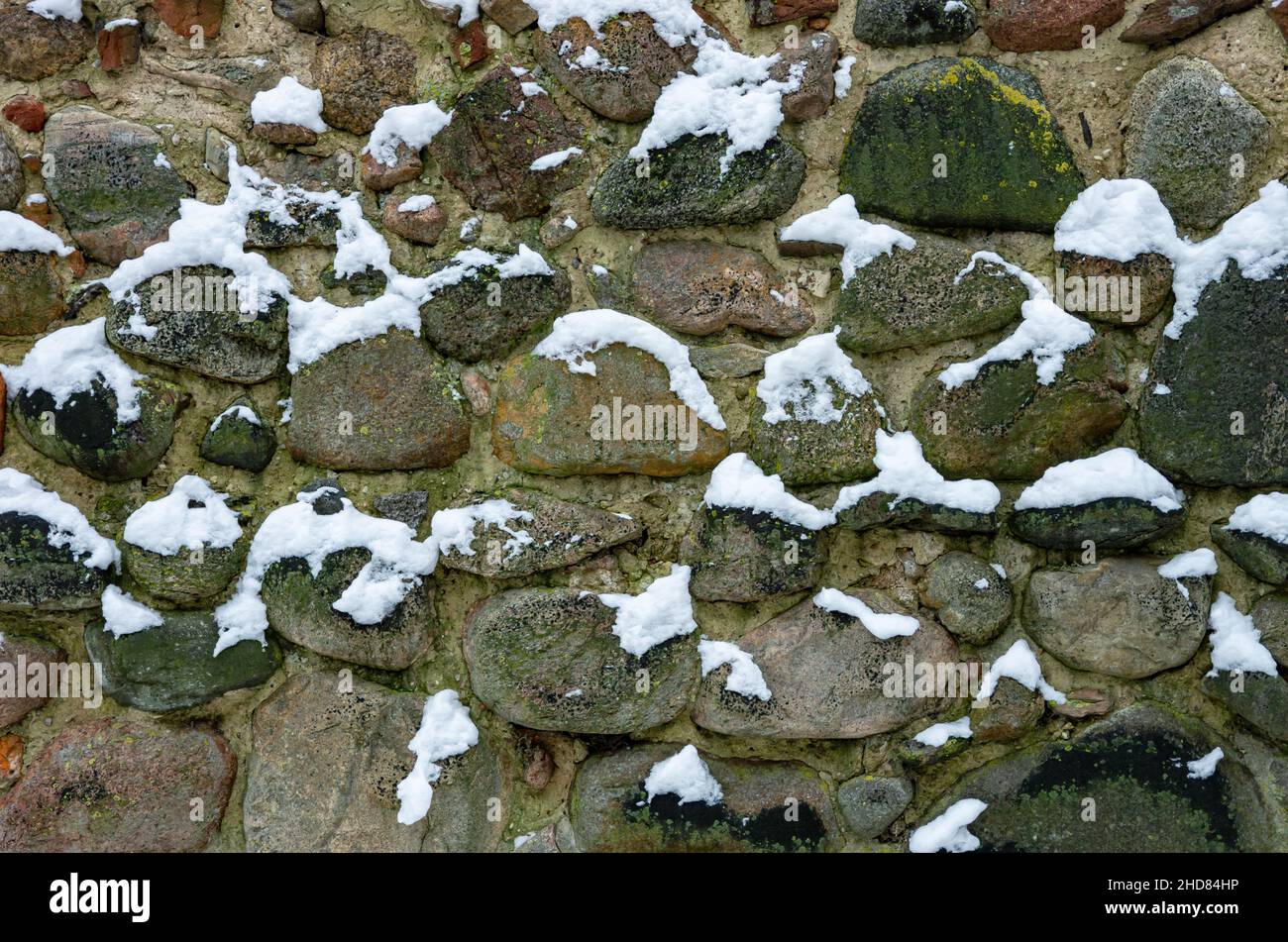 Detail der verschneiten, winterlichen und historischen, mittelalterlichen Stadtmauer aus rauhen Feldsteinen in Neubrandenburg, Deutschland. Stockfoto