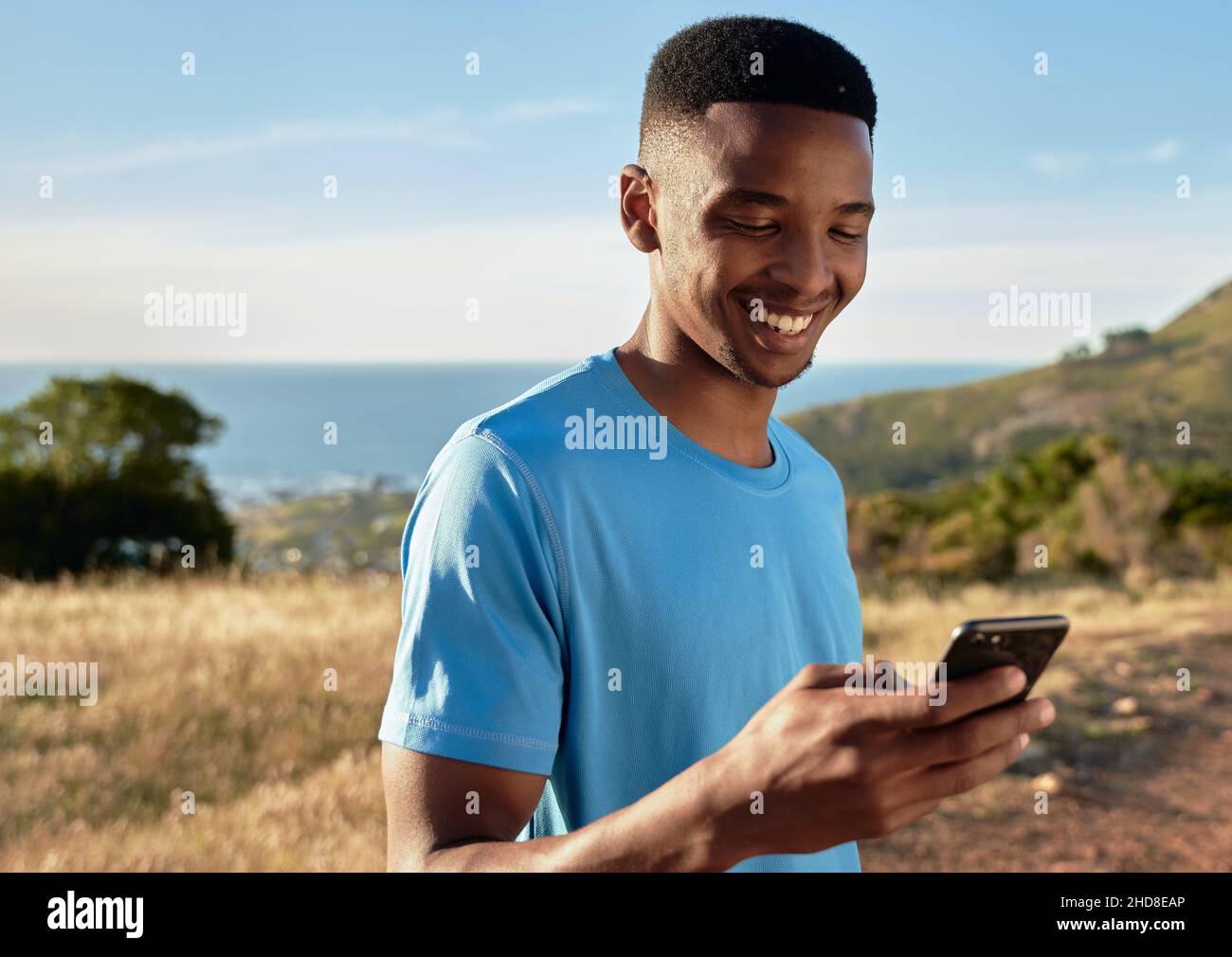 Schwarzer junger Erwachsener, lächelnd, während er sein Handy benutzte, um einen Bergspaziergang zu beginnen. Schöne Aktivitäten im Freien. Stockfoto