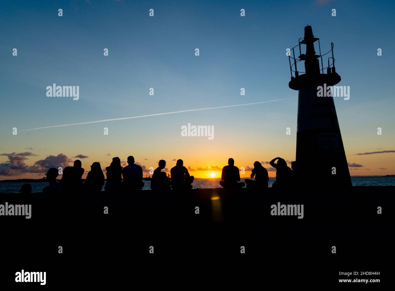 Silhouette einer mittleren Gruppe von Menschen, die den Sonnenuntergang vom Leuchtturm Ponta do Humatia in Salvador, Bahia, Brasilien, genießen. Stockfoto