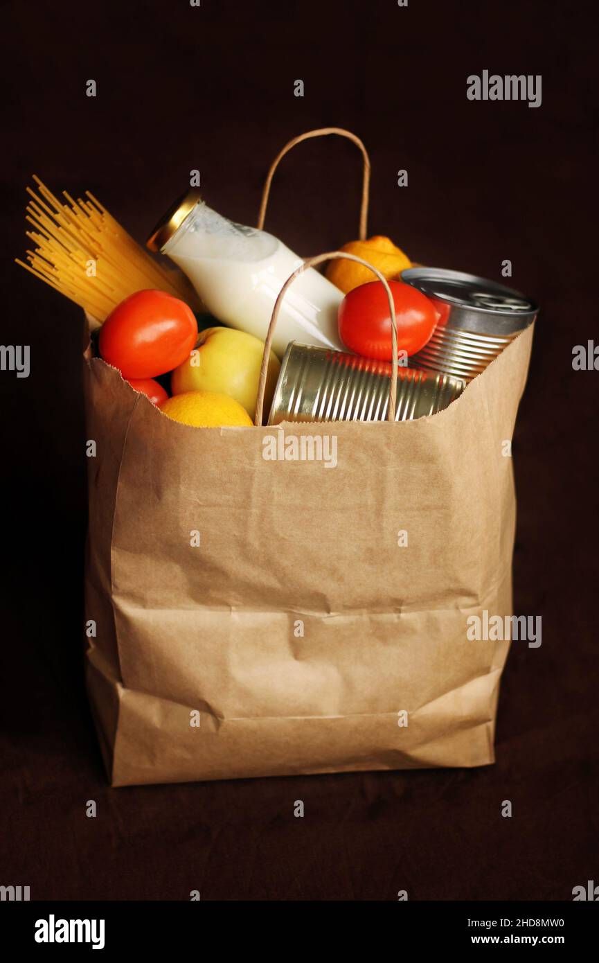 Produkte in einer Papiertüte auf braunem Leinenhintergrund. Essen in einem Paket mit Lieferservice. Konserven, Pasta, Gemüse, Obst, Milch. Kontaktles Stockfoto