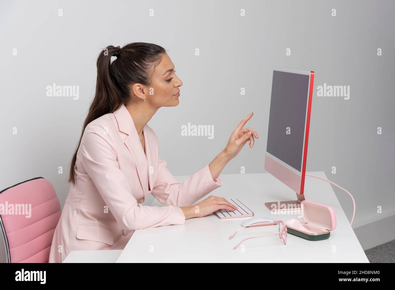 Frau, die mit einer Tastatur und einem Desktop-Computer an einem Arbeitsplatz sitzt. Alle mit einem rosa Thema. Stockfoto