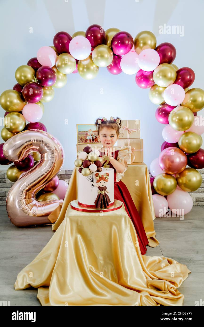 Vertikales Porträt eines süßen zweijährigen kleinen Mädchens, das hinter ihrem Geburtstagskuchen steht und einen Wunsch macht. Schöne Baby Mädchen Geburtstag Fotoshooting Stockfoto