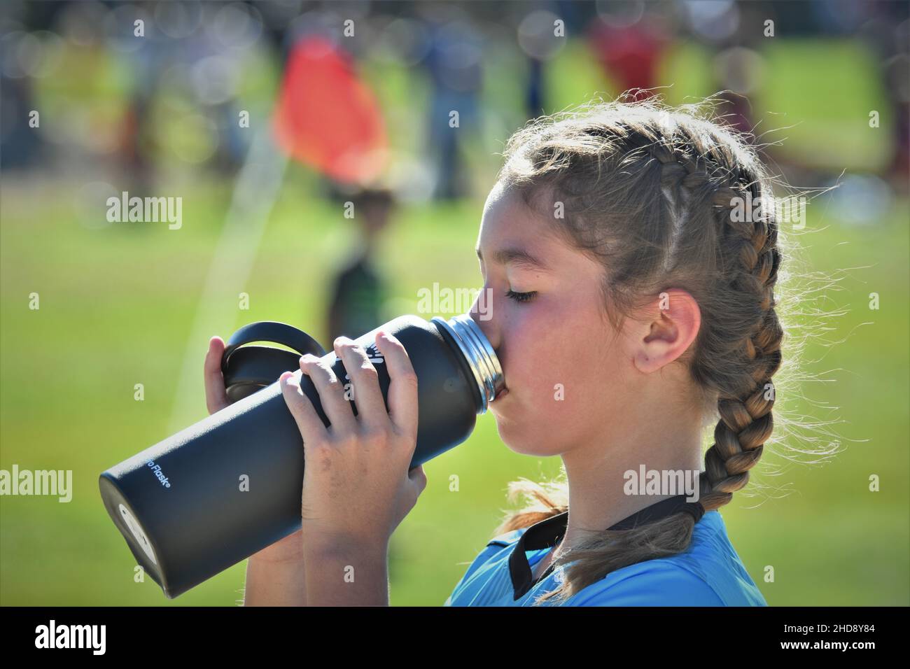 12-Jähriger, der in der Pause bei 101 Grad bei einer halben Fußballspiel-Temperatur mit panierten, ginn- und bob-Haaren aus der Thermoskanne trinkt Stockfoto