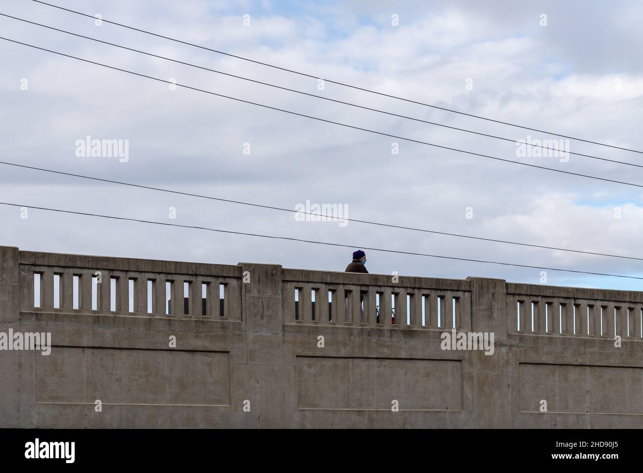 Cambridge, Ontario, Kanada - Oktober 23 2021: Älterer Mann mit blauem Turban und chirurgischer Maske, der über eine Steinbrücke läuft. Hydrolines über Kopf. Stockfoto