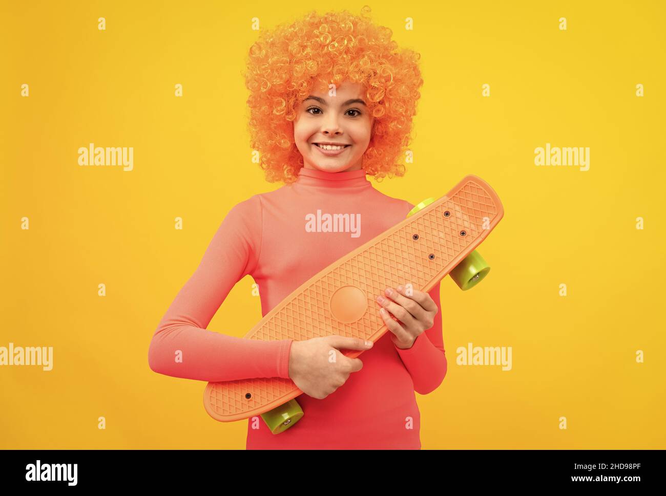 Happy Girl Scater mit orangen Haaren in rosa Poloneck Lächeln hält Pennyboard, Skateboarding Stockfoto