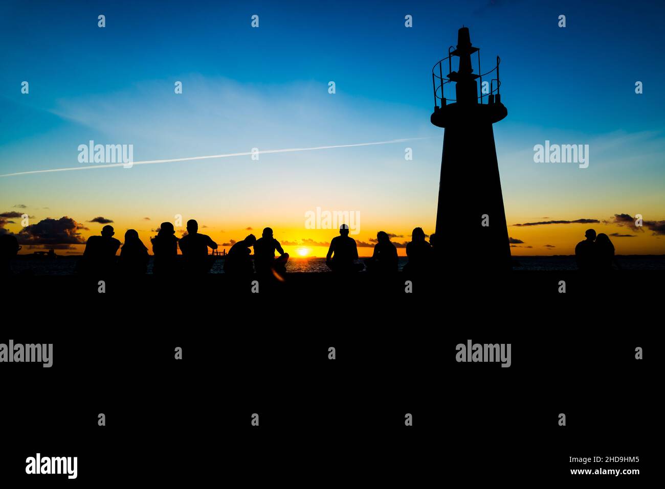Silhouette einer mittleren Gruppe von Menschen, die den Sonnenuntergang vom Leuchtturm Ponta do Humatia in Salvador, Bahi, genießen Stockfoto