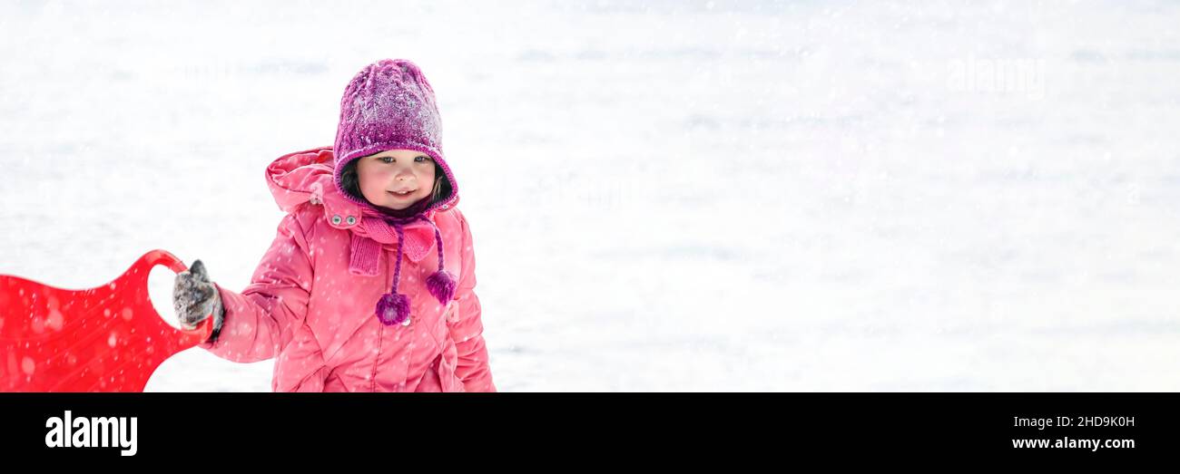 Ein Mädchen in rosa Kleidung reitet im Winter auf einer verschneiten Rutsche. Weißes Mädchen 5 Jahre alt Rodeln im Winter während eines Schneefalls. Stockfoto