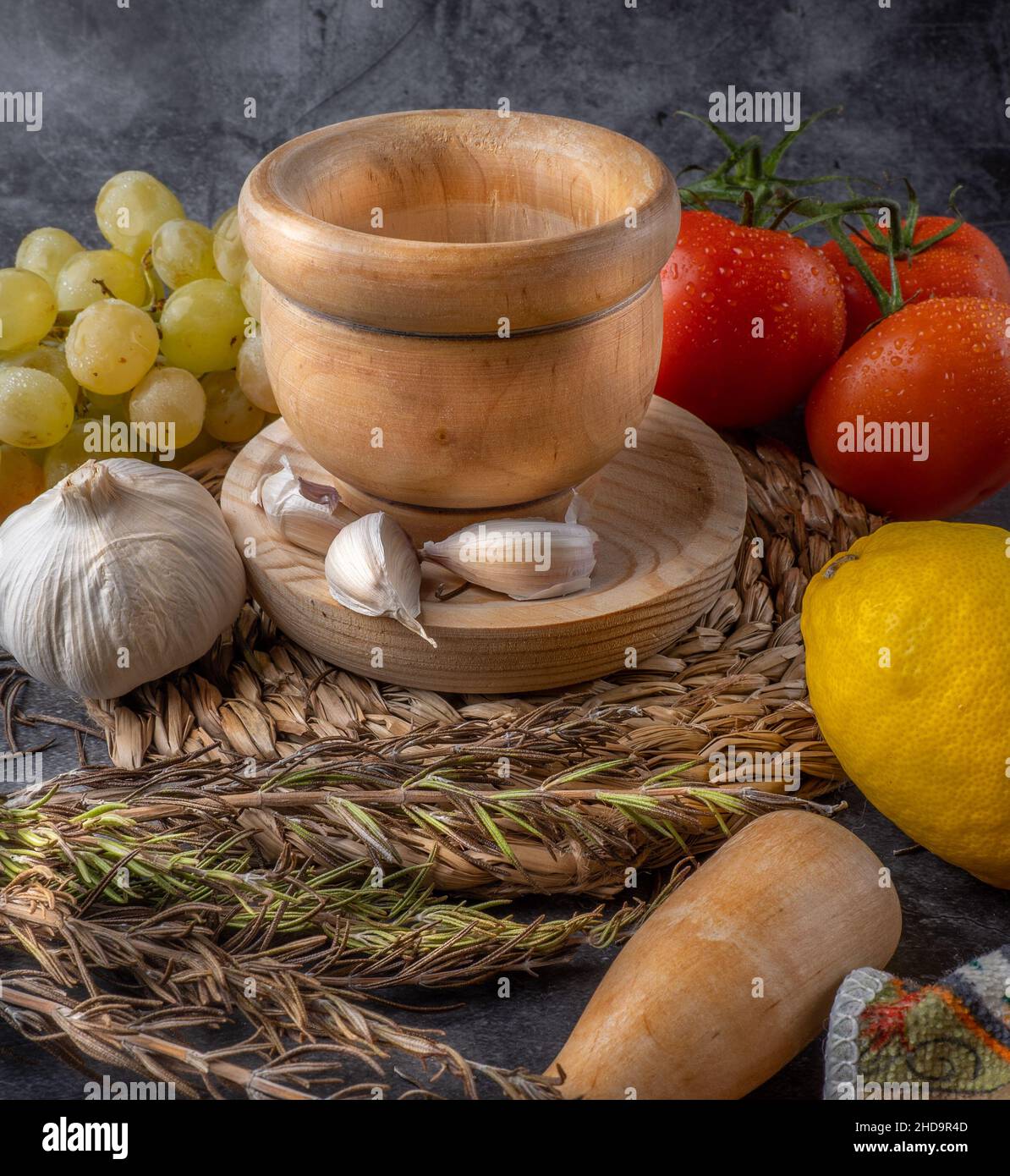 Stillleben, Trauben und Tomaten in abstrakter Zusammensetzung und intensiver Farbe. Szene mit Mörtel zum Zerkleinern von Lebensmitteln in antikem Holzton. Stockfoto