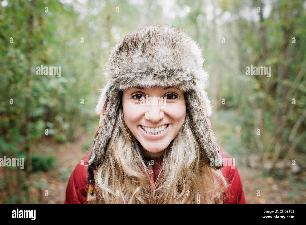 Porträt einer Frau, die einen pelzigen Hut in einem Wald trägt und lächelt Stockfoto