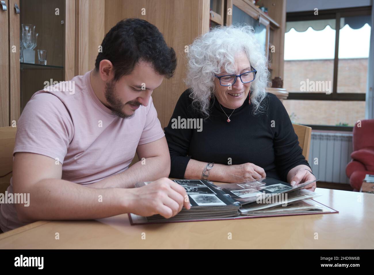 Lächelnde Mutter und ihr erwachsener Sohn schauen sich gemeinsam alte Fotos an. Stockfoto