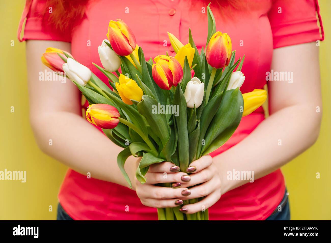 Die junge Frau hält einen großen Strauß Tulpen in ihren Händen auf gelbem Hintergrund. Geschenk für den Frühlingsurlaub. Stockfoto