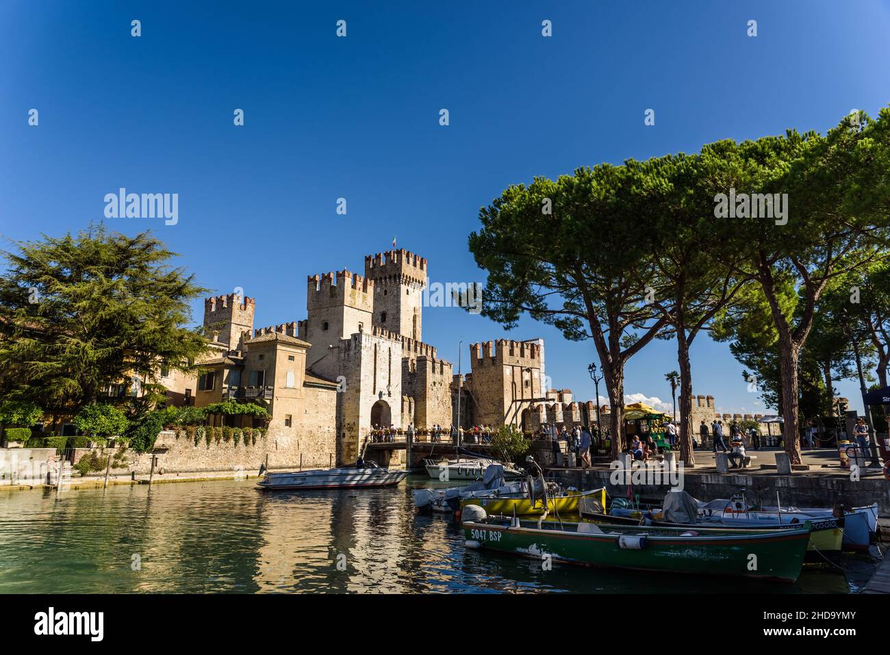 Sirmione, Italien - 28. September 2021: Boote, die neben dem Schloss Sirmione am Gardasee festgemacht sind, werden im Sommer von Touristen bewundert. Stockfoto