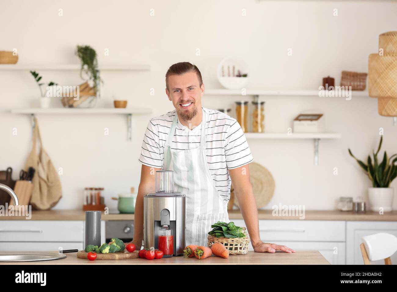 Junger Mann mit frischem Gemüse und modernem Entsafter in der Küche Stockfoto