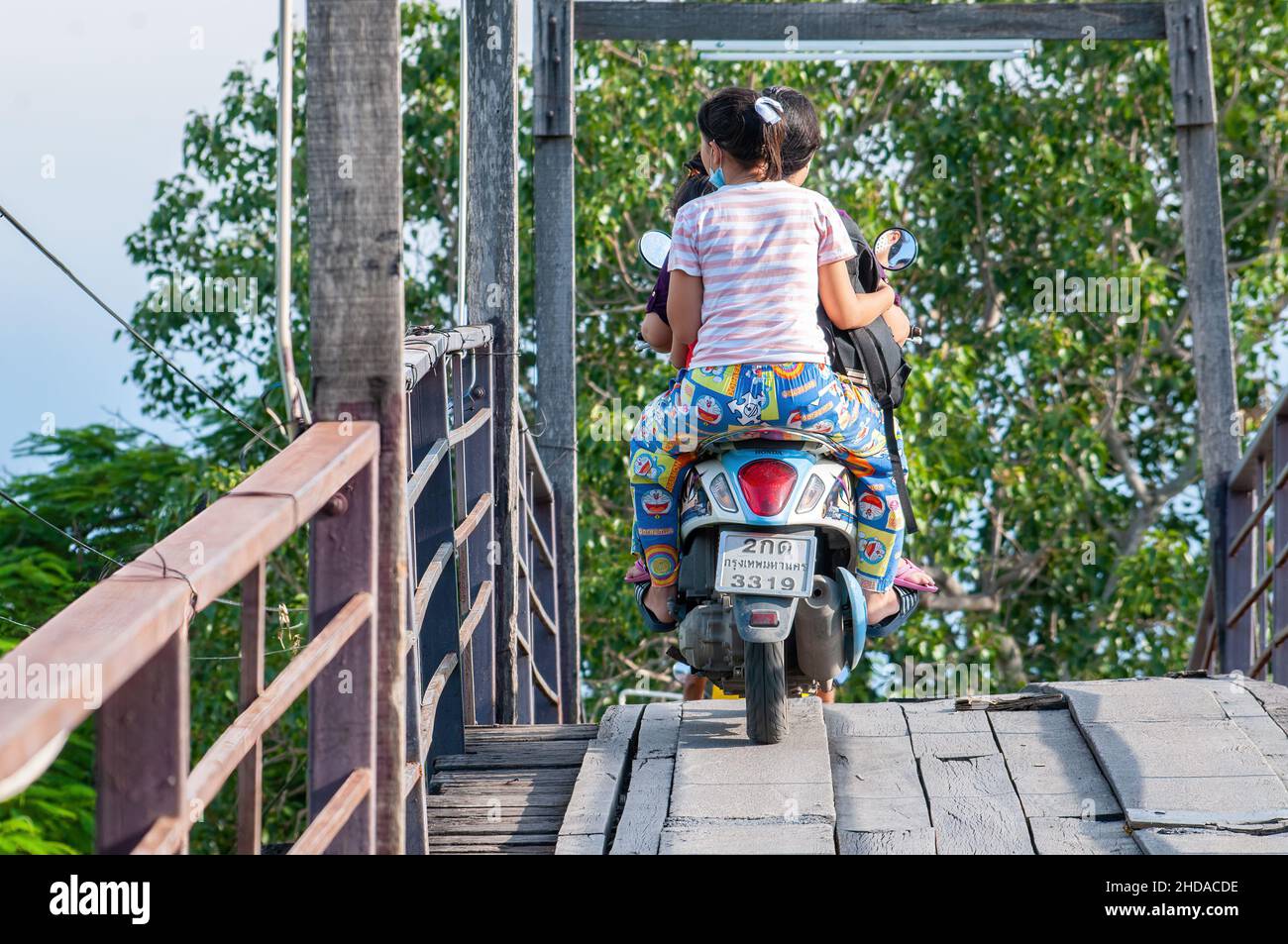 Motorrad mit drei Personen, die eine Holzbrücke über einen Kanal in Bangsaothong, Provinz Samut Prakan in Thailand, überqueren. Stockfoto