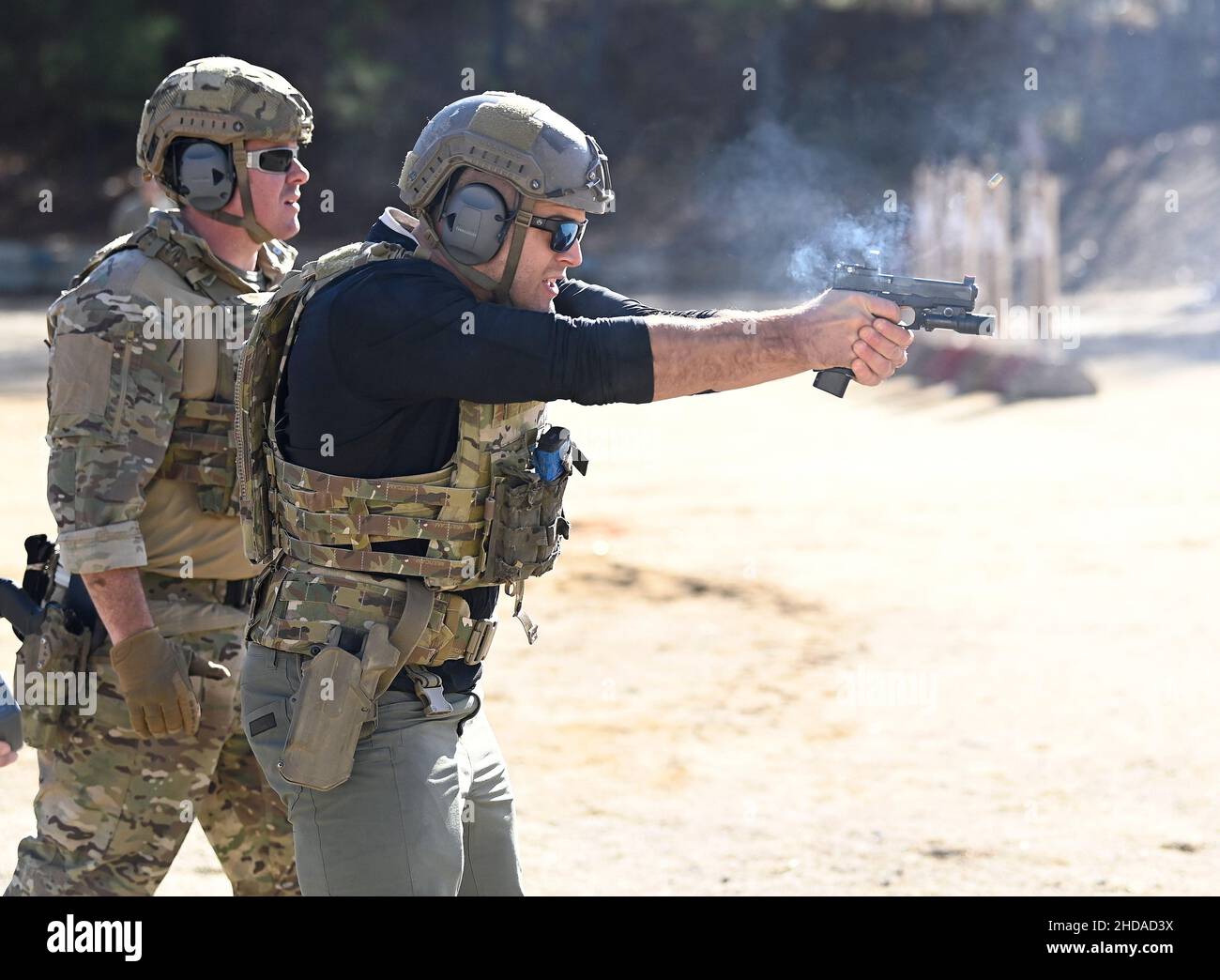 Crossfitter Jacob Hepner feuert eine Pistole auf Ziele, während ein Green Beret während der Celebrity Tactical Challenge 2021 im John F. Kennedy Special Warfare Center der US-Armee und im Miller Training Complex der Schule am 16. Dezember 2021 anschaut. Zwölf Prominente haben sich mit Green Berets zusammengetan, um an der jährlichen Veranstaltung teilzunehmen. (USA Armeefoto von K. Kassens) Stockfoto