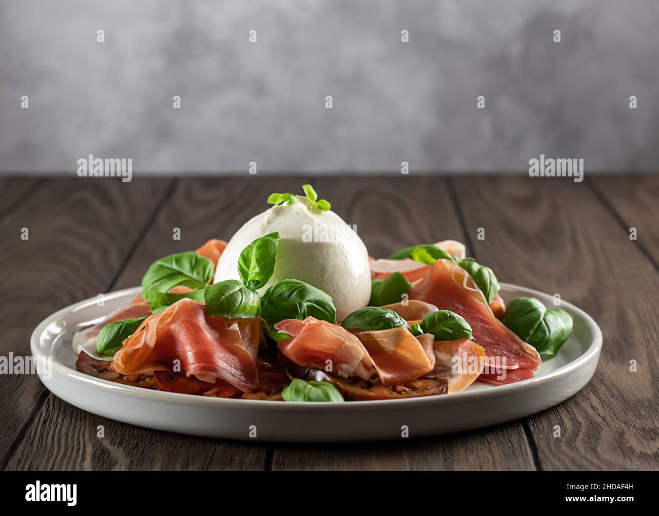 Selektiver Fokus auf italienischen Prosciutto mit Burrata-Käse, frischem Basilikum, Tomaten. Geringe Schärfentiefe. Stockfoto