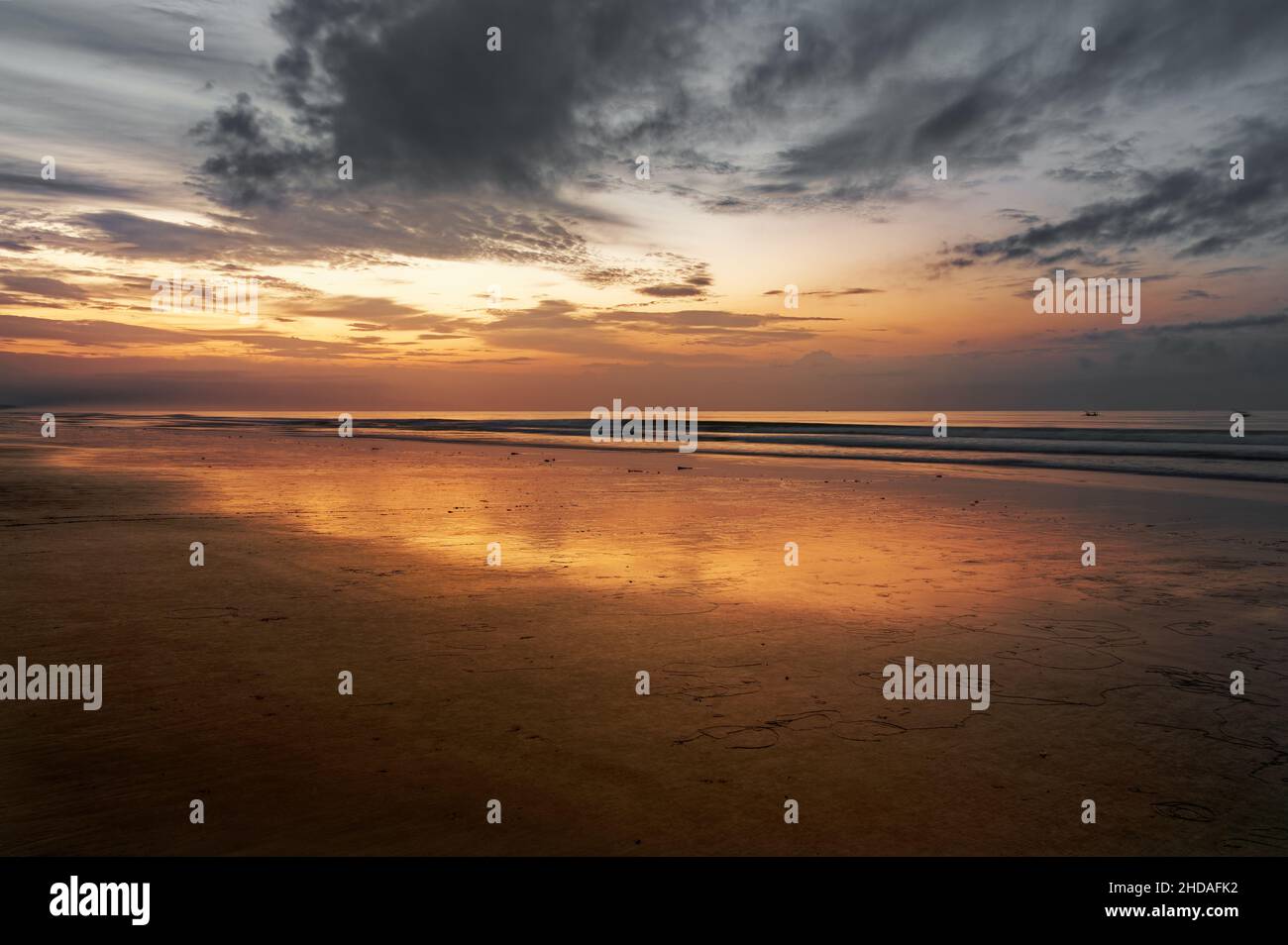 Spektakulärer Blick auf die Küste eines Bali Strandes, bei Sonnenaufgang mit einem sehr dunklen bewölkten Himmel, aber mit einem Sonnenlicht, das eine wunderschöne orangefarbene Reflexion bietet. Stockfoto