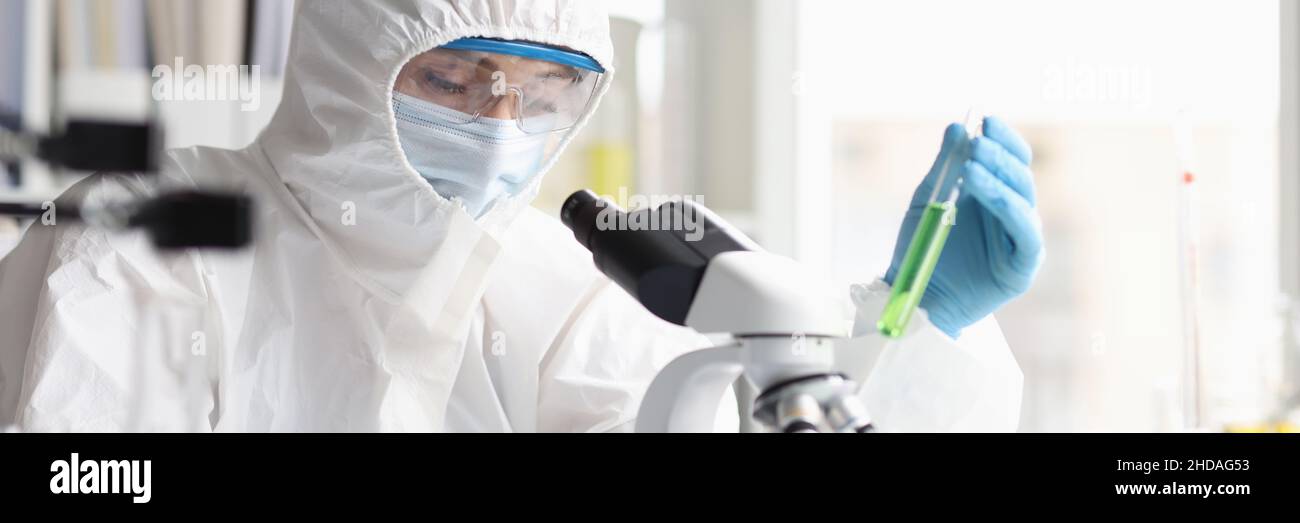 Eine Chemikerin im Schutzanzug führt Laboruntersuchungen zu grüner Flüssigkeit durch Stockfoto