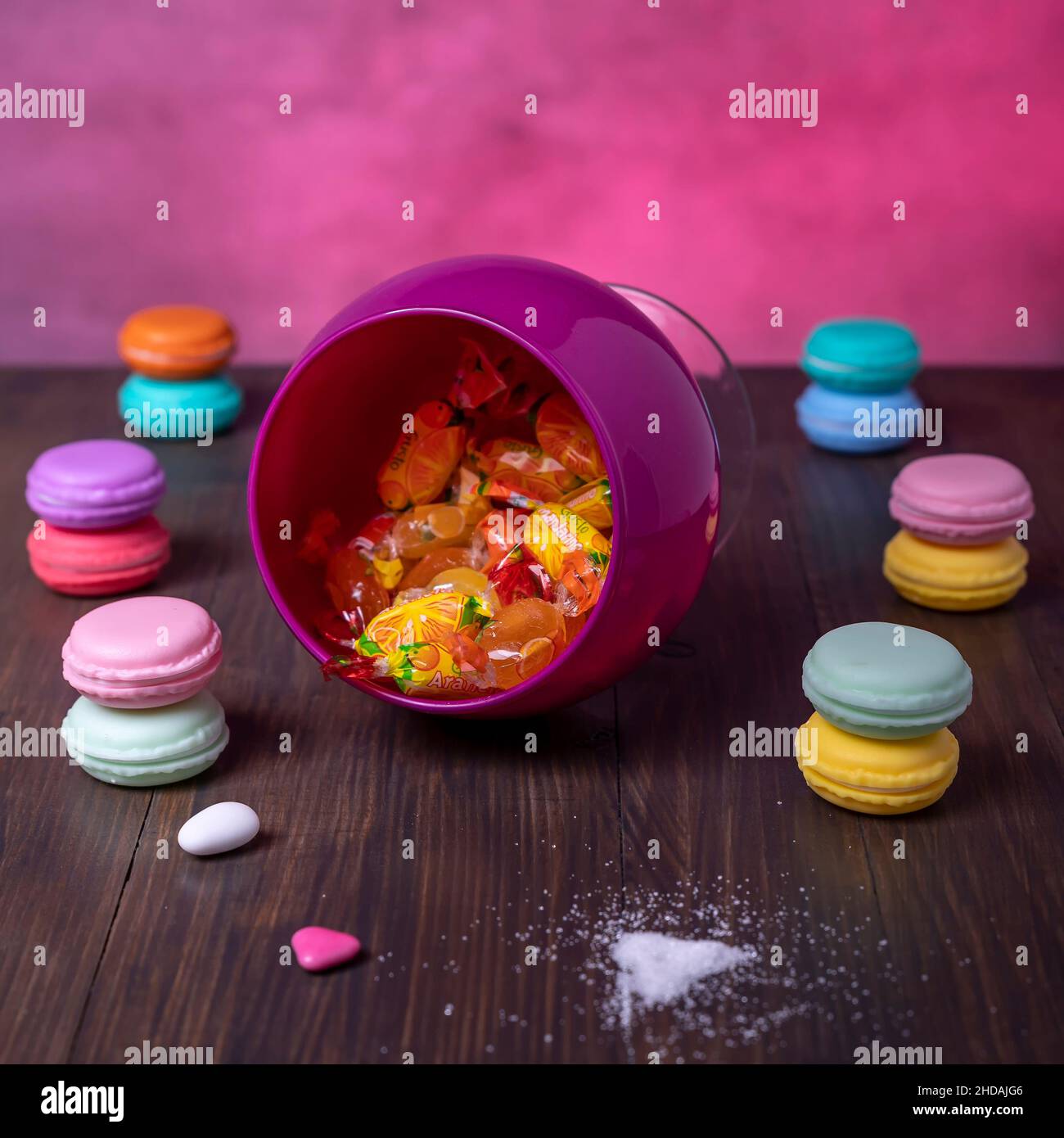 Zusammensetzung von Bonbons in einem umgedrehten Glasbehälter und Paaren von übereinander liegenden bunten Makronen Stockfoto