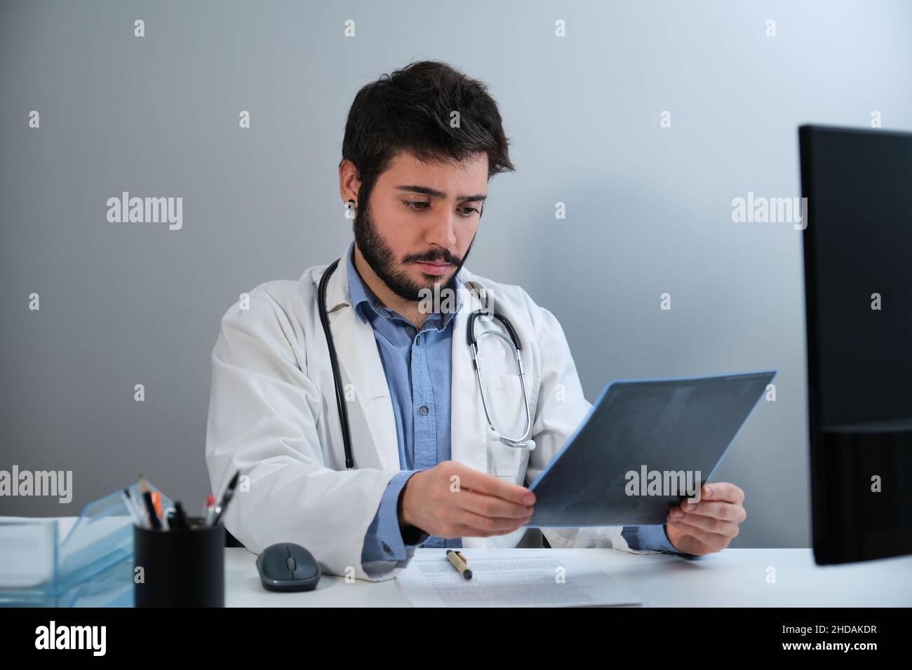 Junger Arzt, der eine Röntgenaufnahme eines Beckens und einer Wirbelsäule am Schreibtisch ansieht. Stockfoto