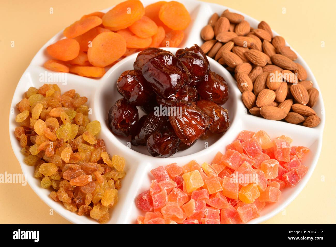 Mischung aus getrockneten Früchten und Nüssen auf einem weißen Teller. Aprikose, Mandel, Rosinen, Datteln Frucht. Auf einem beigen Hintergrund. Platz für Text oder Design. Stockfoto