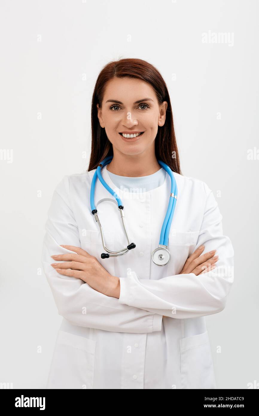 Lächelnde Ärztin mit überkreuzten Armen stehend und in die Kamera blickend, isoliert auf weißem Hintergrund. Medizinisches Berufskonzept Stockfoto