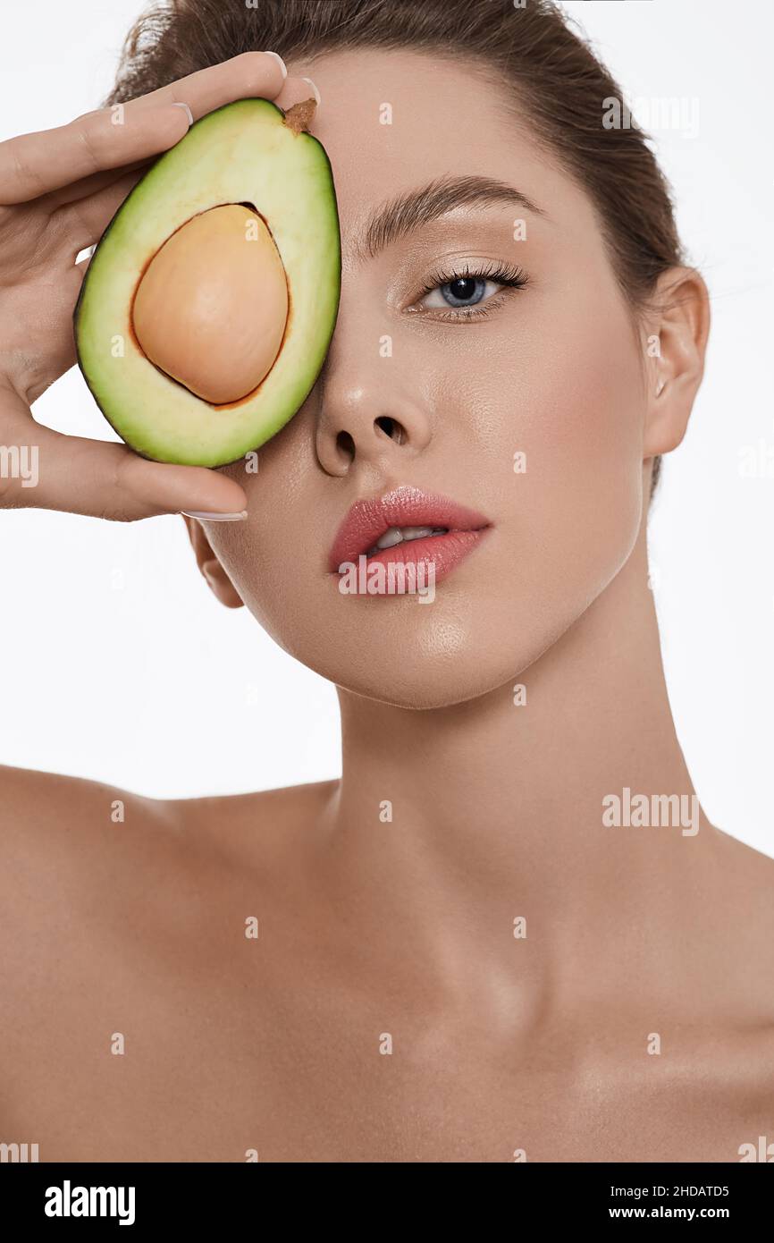 Feuchtigkeitsspendend und Pflege der Haut mit Kosmetik mit Avocado. Frau hält Avocado in der Nähe ihres frisch glühenden, hydratisierten Hautgesichts Stockfoto