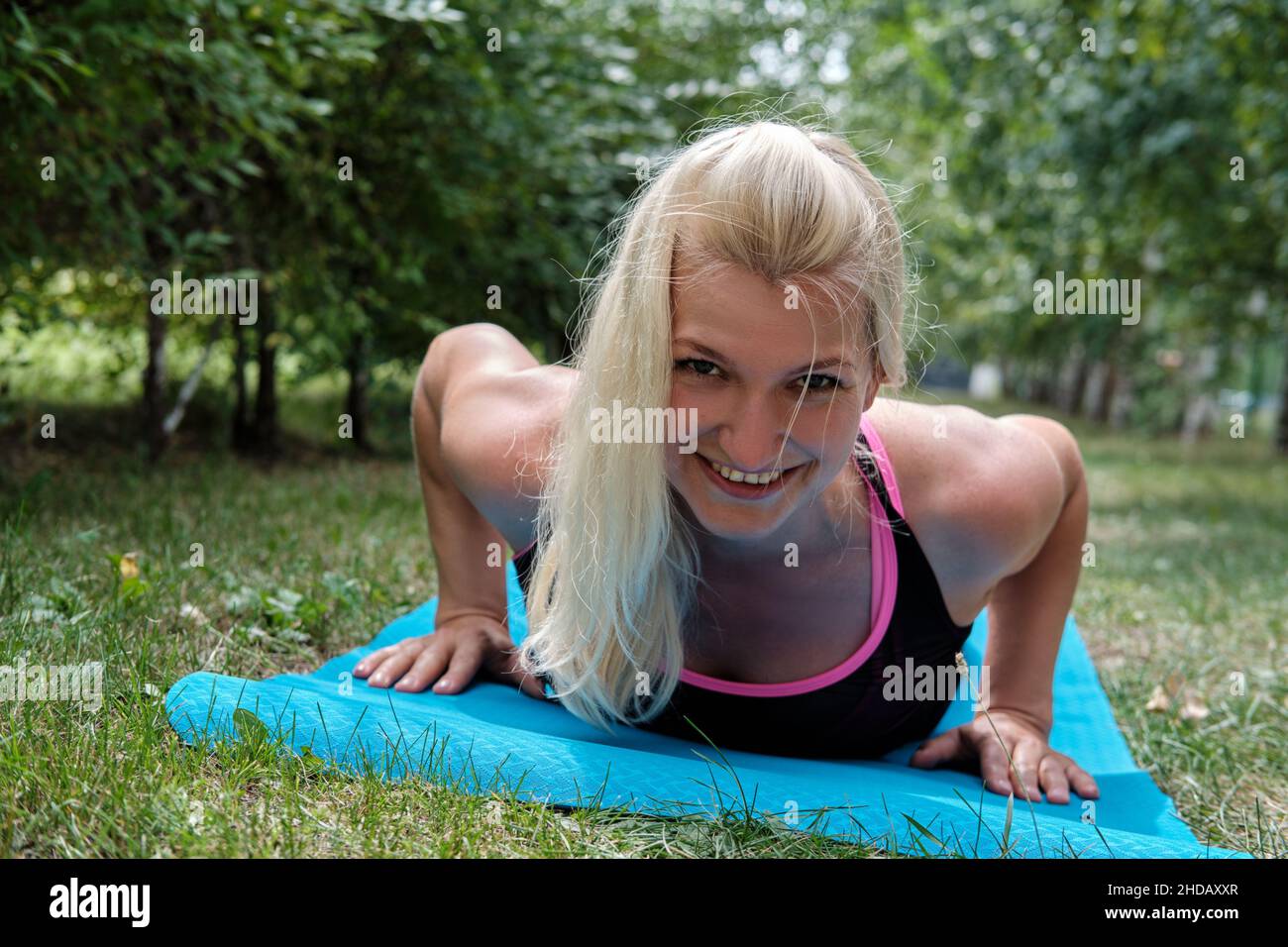Positive blonde Frau macht Liegestütze beim Training im Park. Fitness im Freien. Stockfoto