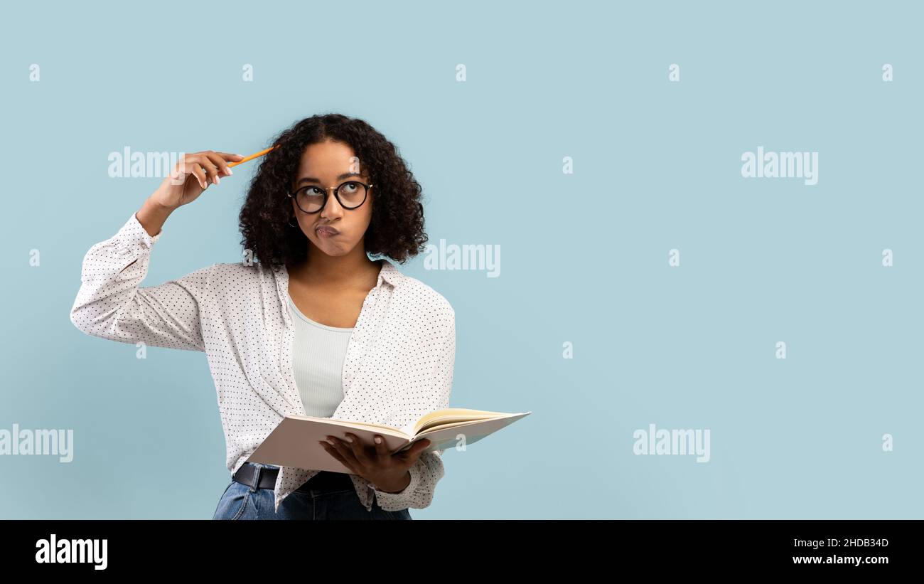 Nachdenkliche junge schwarze Studentin liest Buch, denkt über etwas auf blauem Hintergrund, Banner mit Kopierraum Stockfoto